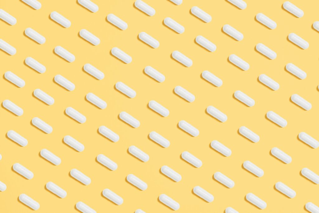 Pattern of white capsules on a bright yellow surface, symbolizing healthcare and medicine.