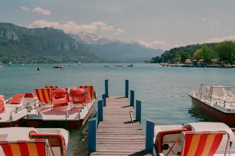 Explore the tranquil beauty of Lake Annecy with docked pedal boats and stunning mountain views.